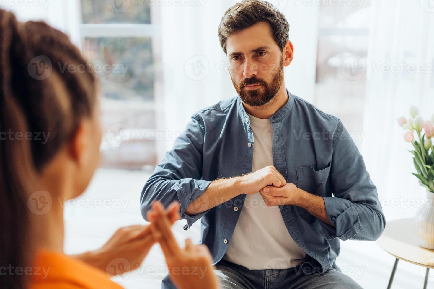 Pensive man and Latin woman, translator, sitting on sofa at home, speaking with sign language photo