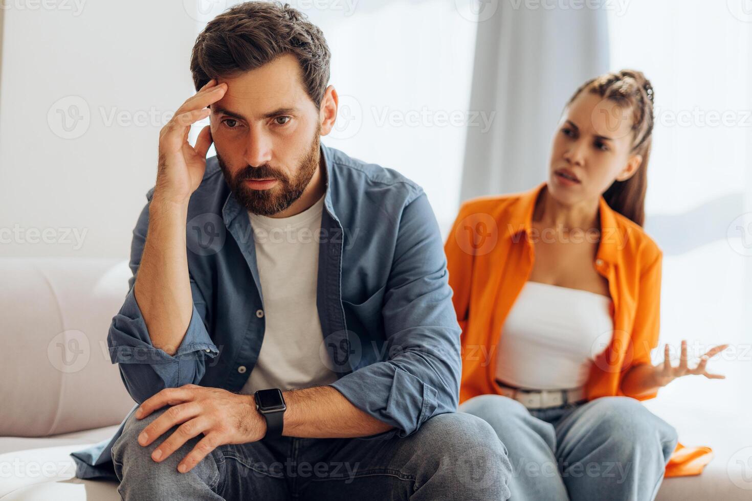 Portrait of sad man being yelled at by angry, abusive woman, sitting on sofa in room at home photo