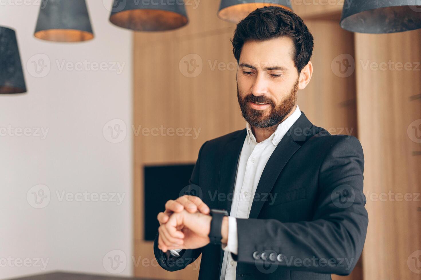 Pensive attractive man, businessman wearing suit looks at the clock, late working in modern office photo