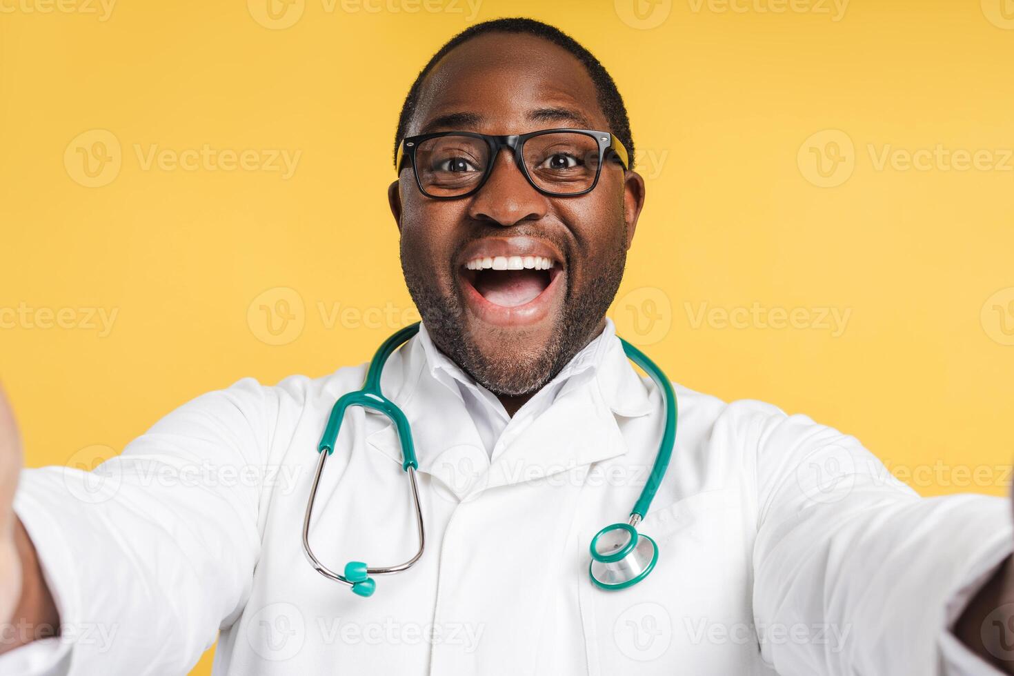 Smiling African American man with stethoscope and glasses, wearing white coat in studio photo
