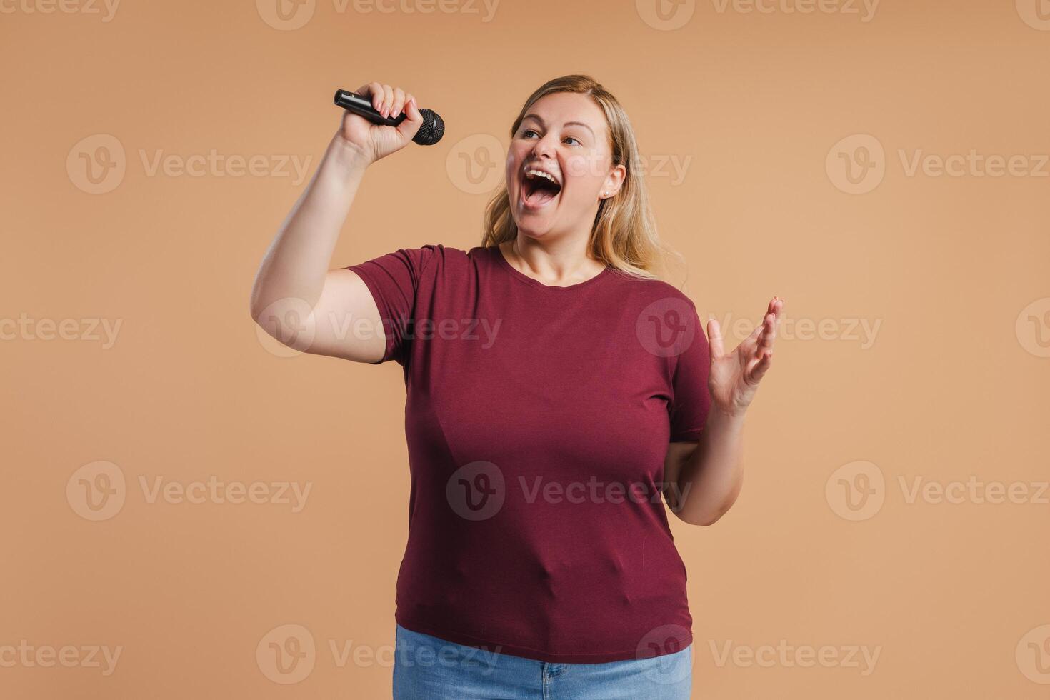 Plus size woman singing loudly into a mic posing in studio photo