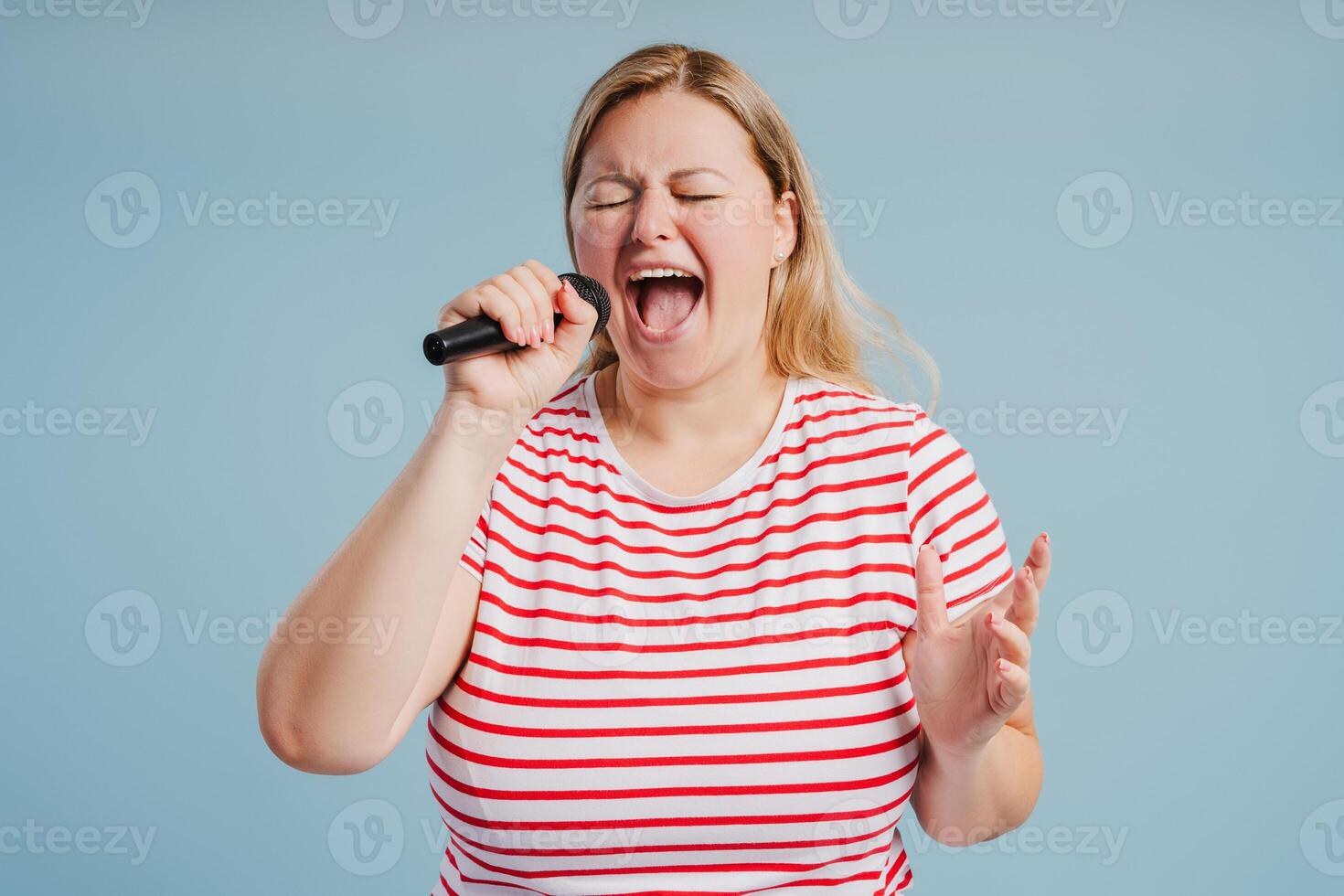Beautiful young woman singing with microphone on blue background photo