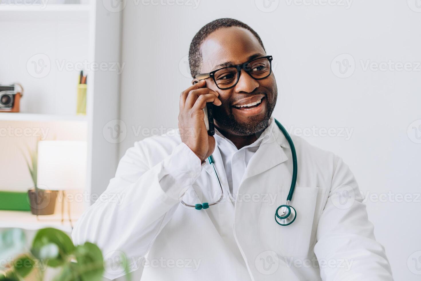 Smiling African American doctor in glasses talking on mobile phone in his office photo