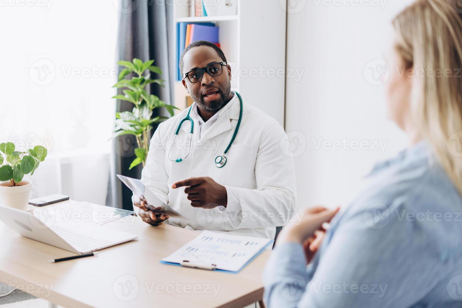 African American doctor in glasses holding x-ray picture talking with female patient photo