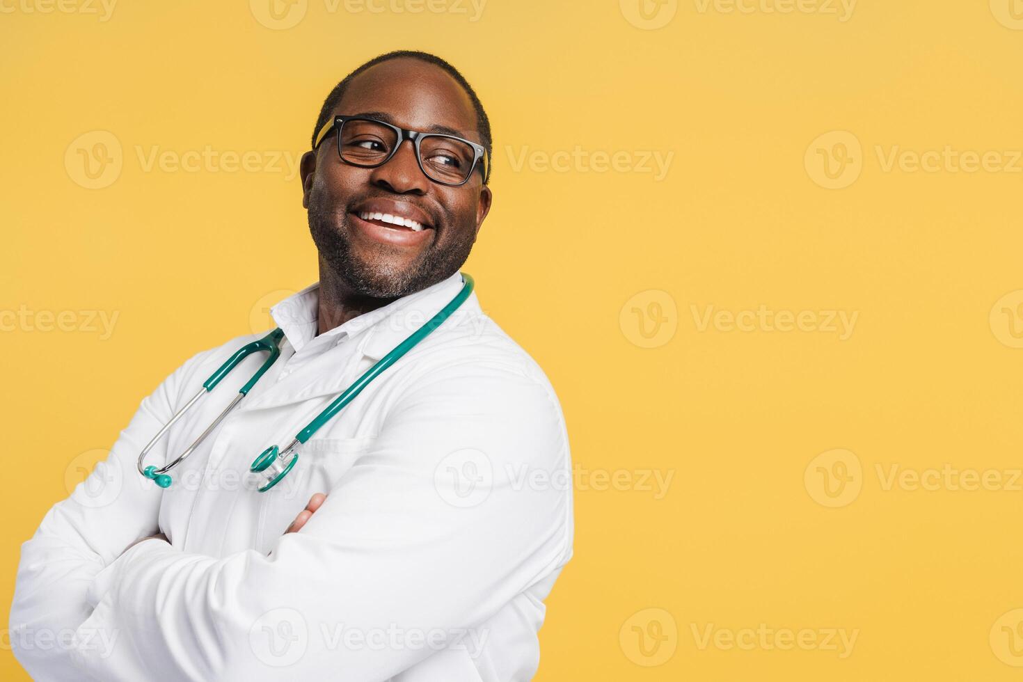 Positive African American doctor in glasses wearing white coat looking at copy space in studio photo