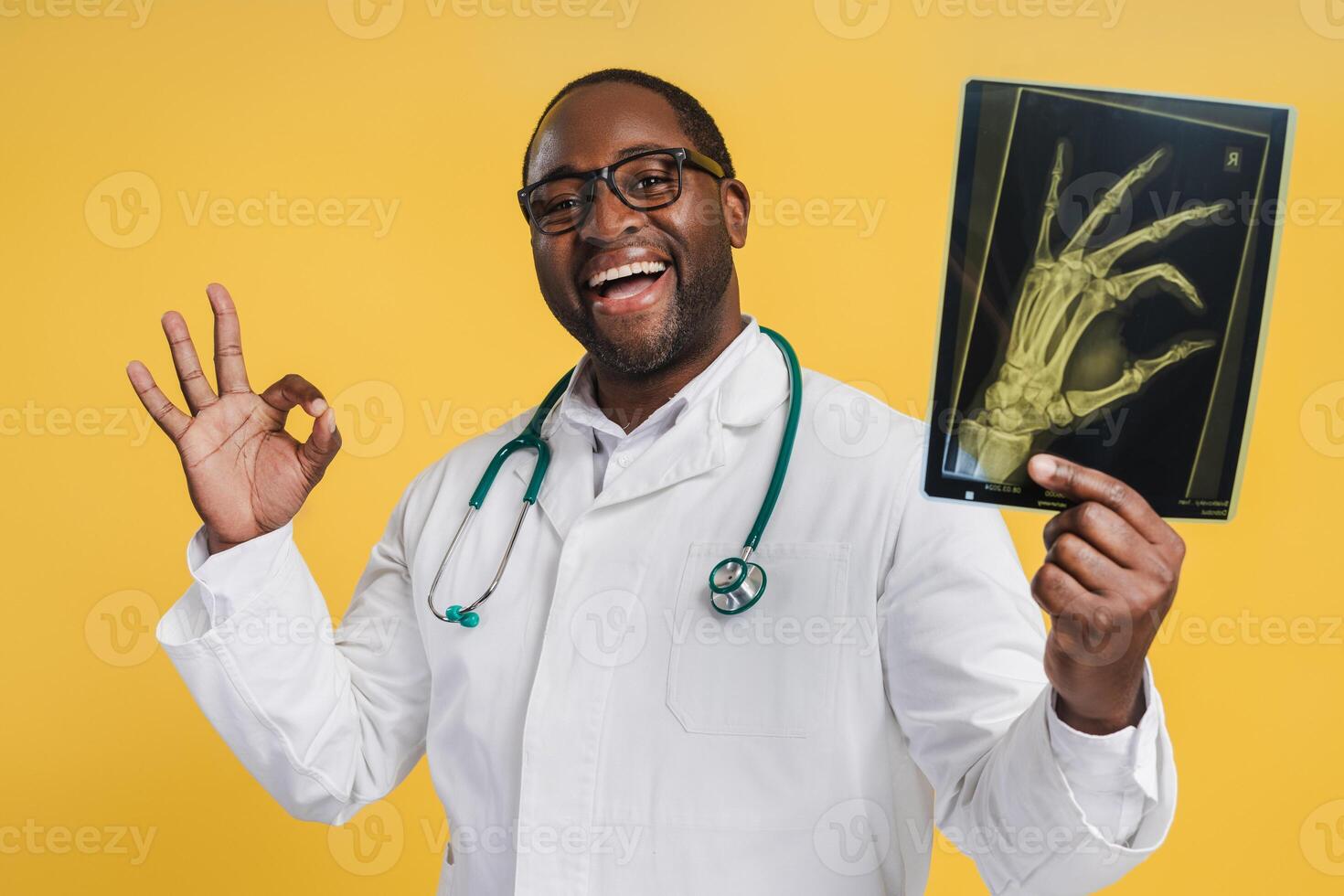 Smiling African American doctor holding X-ray picture with ok gesture, isolated on yellow photo