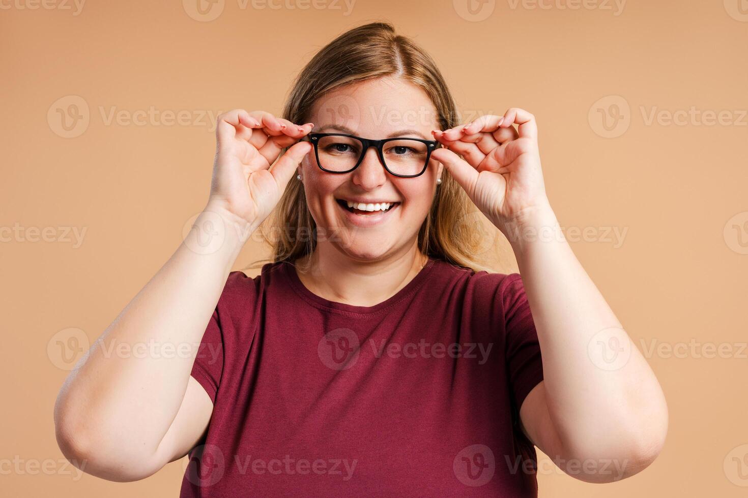 Happy young plus size woman touching her glasses looking at camera in studio photo