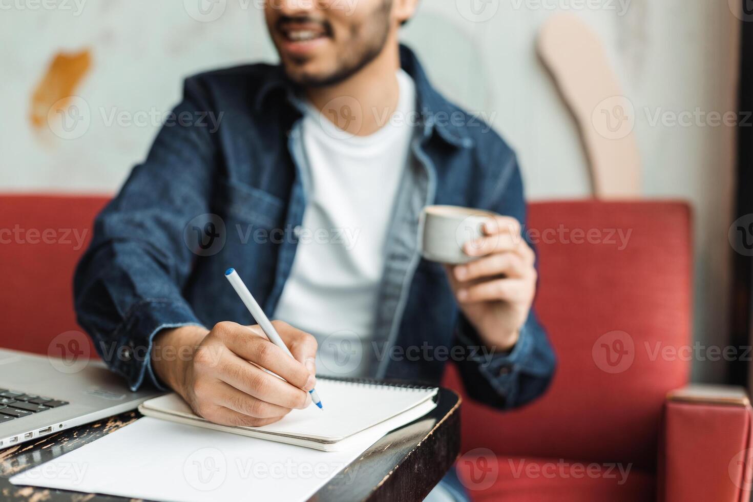 Young man writing on notepad and drinking coffee in cafe photo