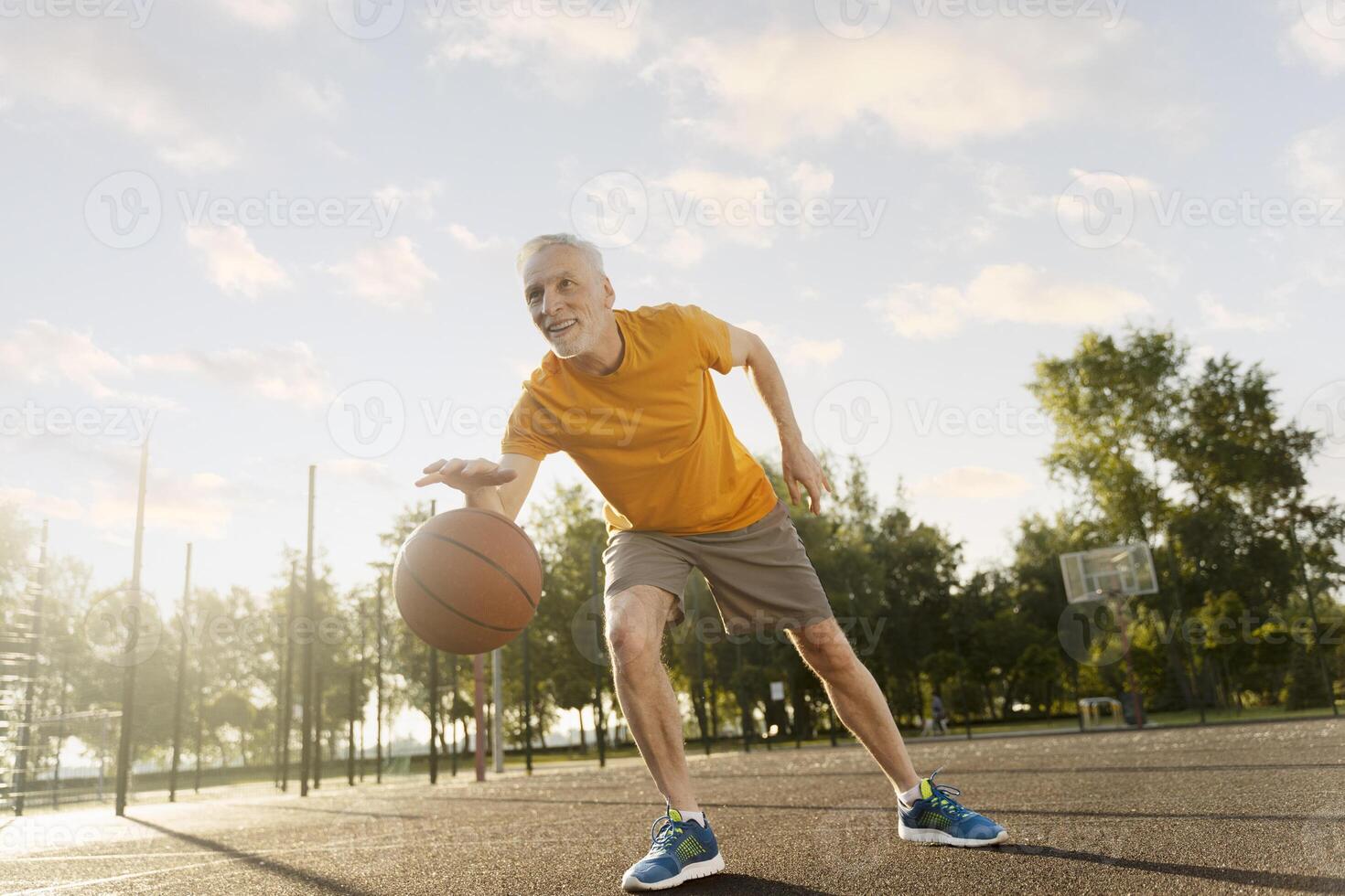 Senior man playing basketball on outdoor court at sunset, photo