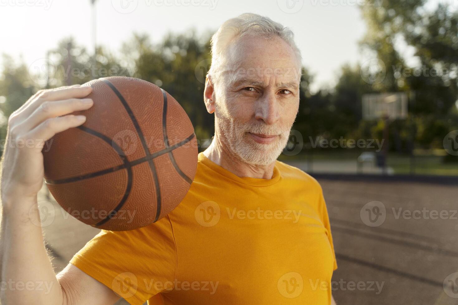 Senior man holding basketball on outdoor court, active retirement lifestyle photo