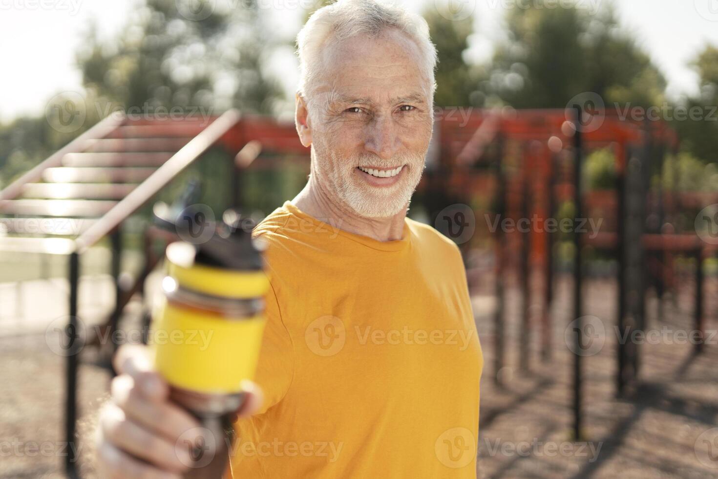 Senior man showing water bottle at outdoor gym promoting hydration and fitness photo