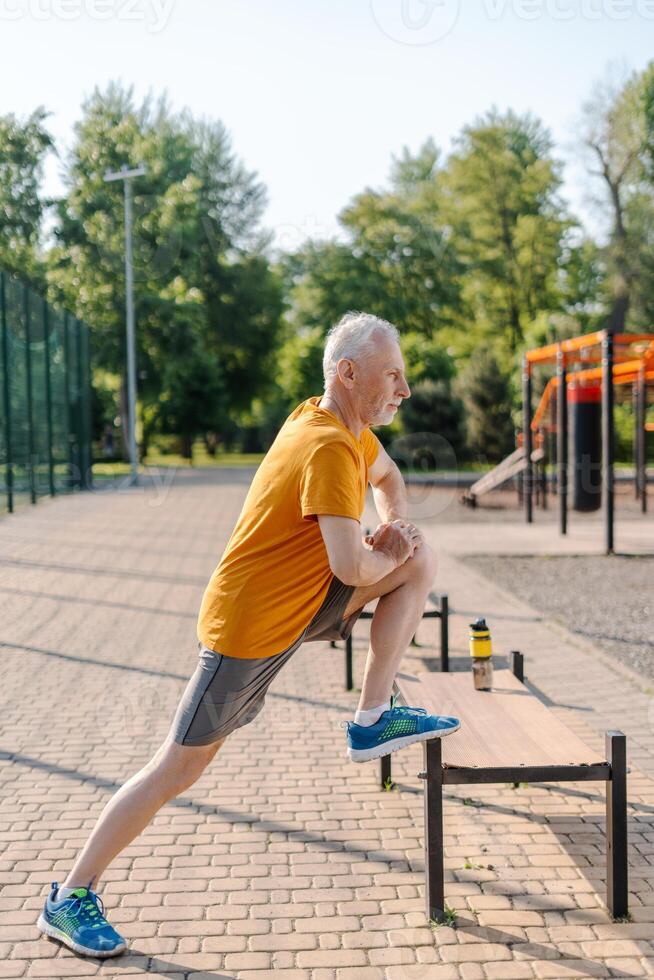 Senior man stretching legs on bench in park before workout photo