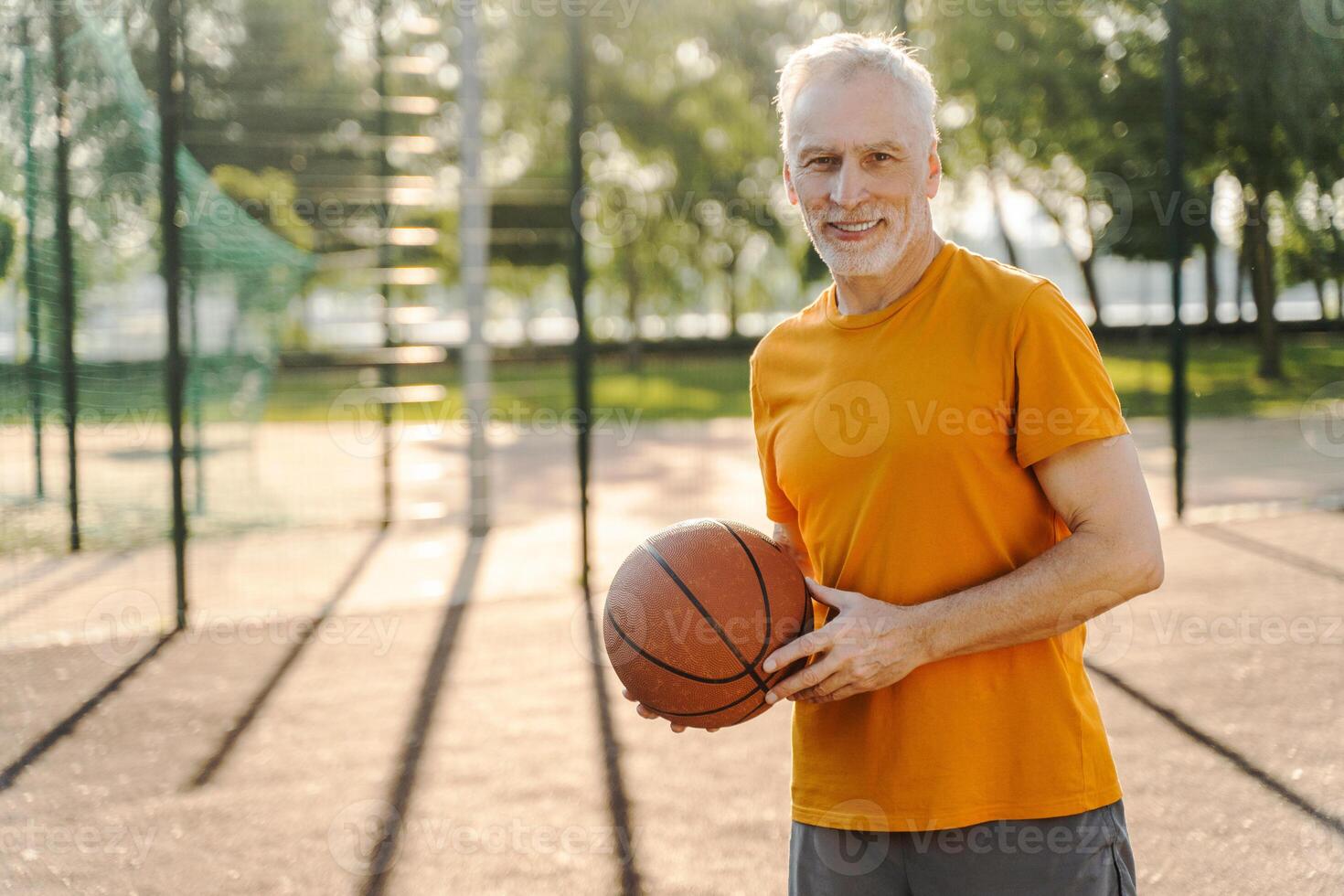Grey haired sportsman holding basketball ball smiling on court photo