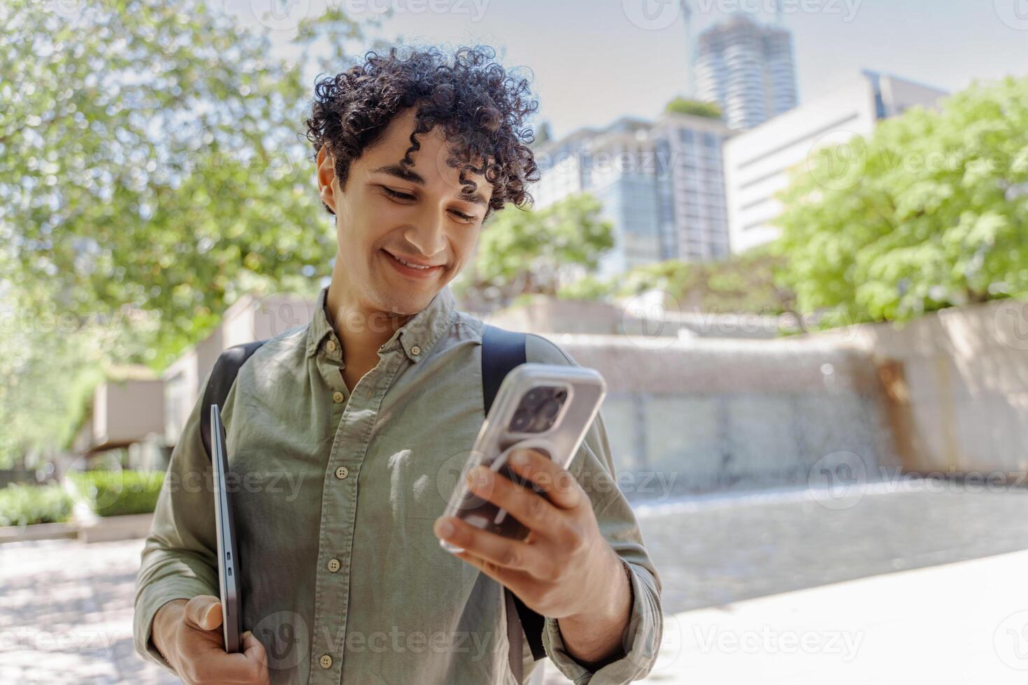 Smiling student walking and using smartphone in urban setting photo