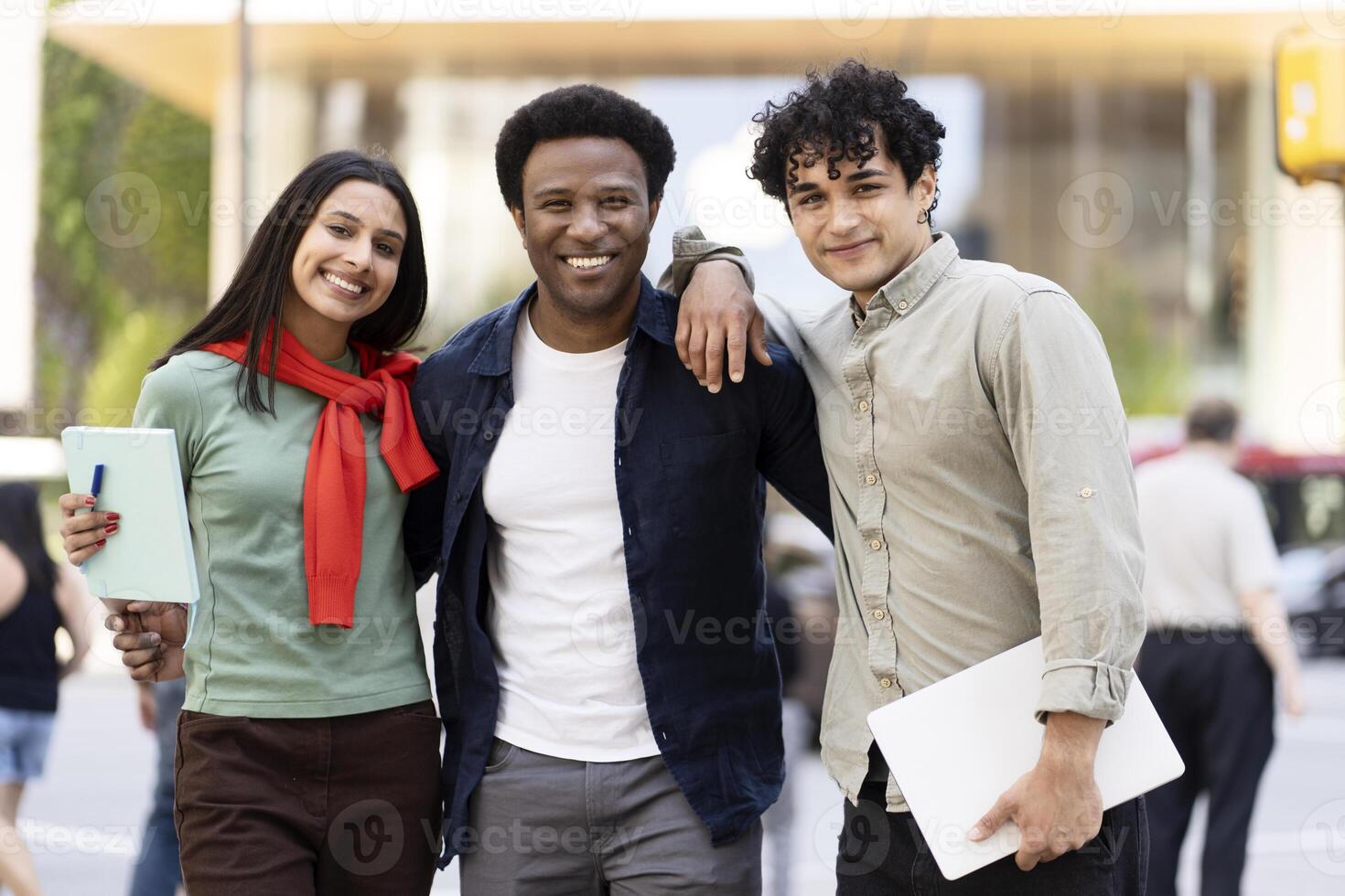 Three happy students smiling outdoors holding books and laptop photo