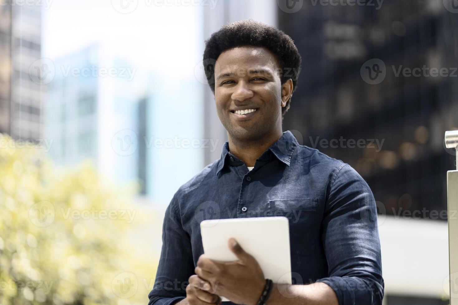 Young professional smiling while holding digital tablet outside office building photo