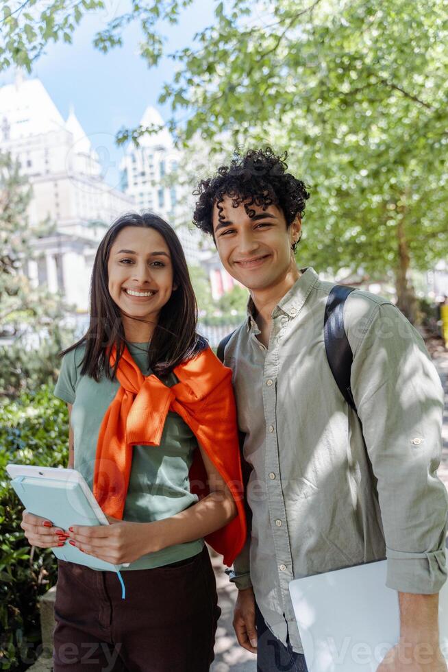Two smiling students walking outside with books and technology photo