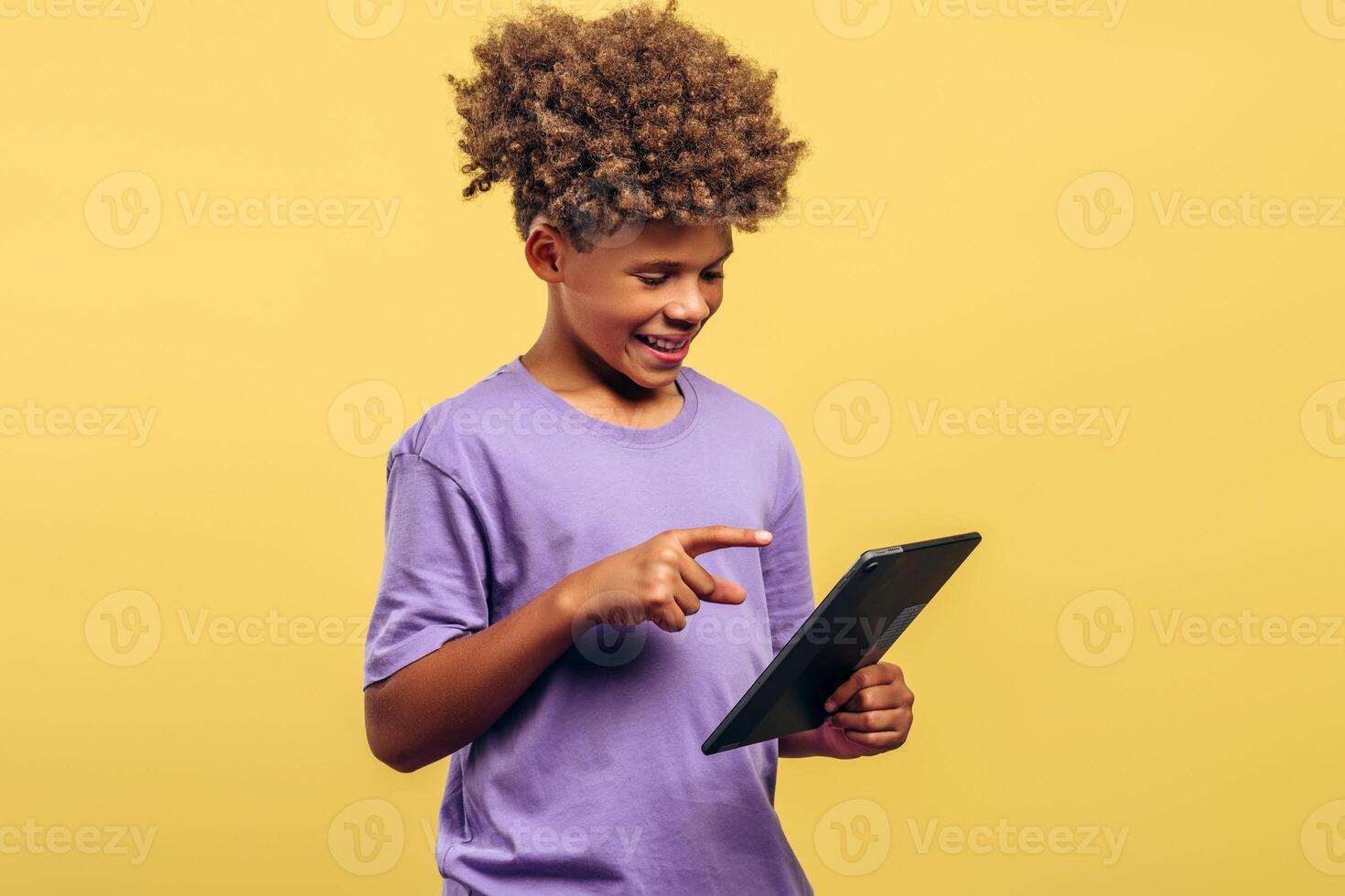 Smiling, attractive African American boy with curly hair holding digital tablet, using mobile app photo