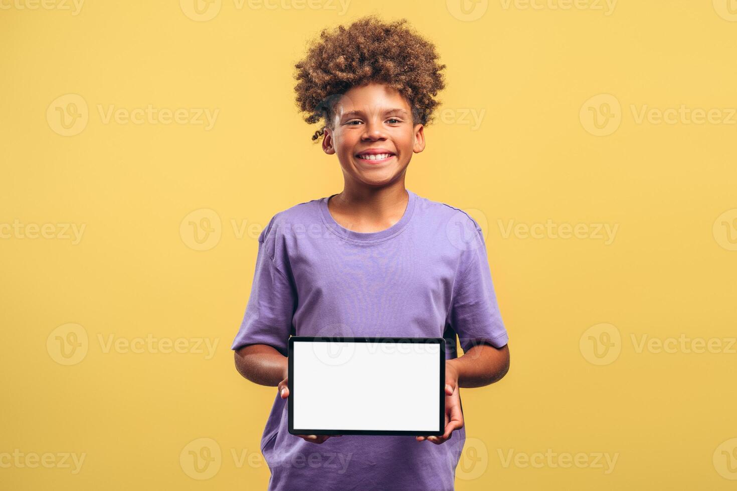 Attractive, smiling African American boy with curly hair holding digital tablet with empty screen photo