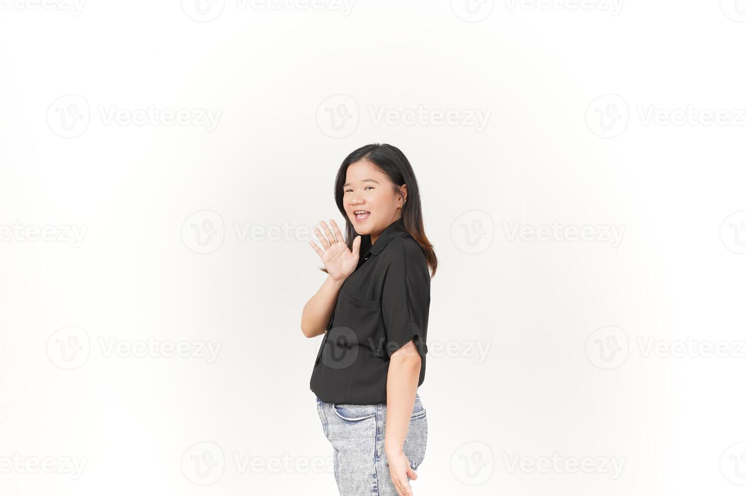 hermosa asiático mujer sonrisas calurosamente, levantamiento su mano en un simpático 'Hola' gesto en contra un blanco antecedentes foto