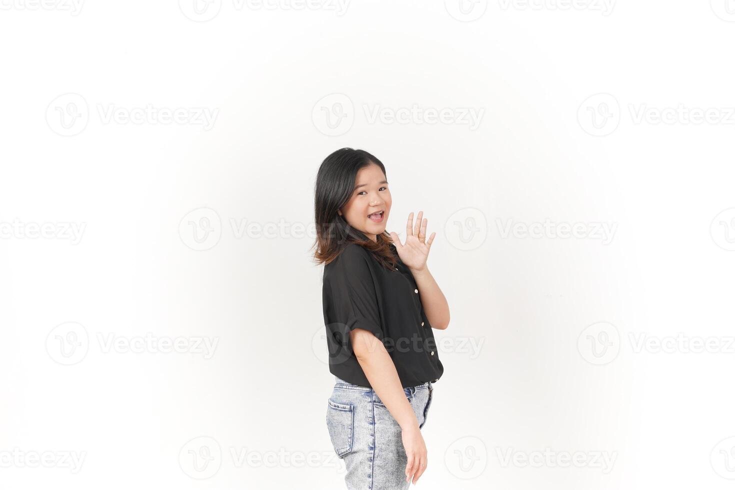 beautiful Asian woman smiles warmly, raising her hand in a friendly 'hi' gesture against a white background photo