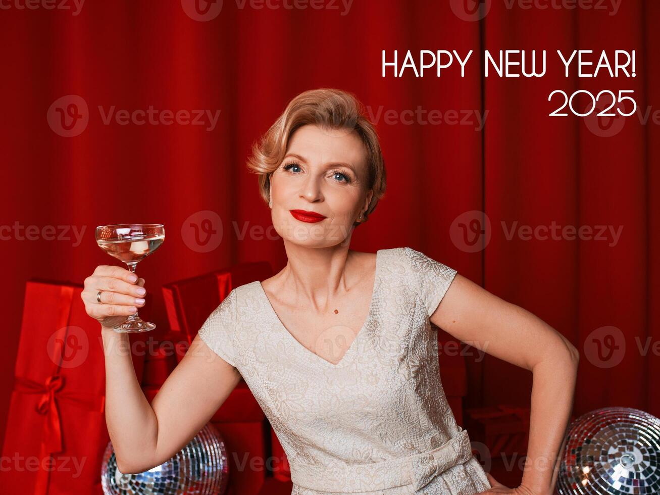 mature stylish elegant woman in cocktail dress with glass of sparkling wine with presents on red background. Party, fashion, celebration, anti age concept photo
