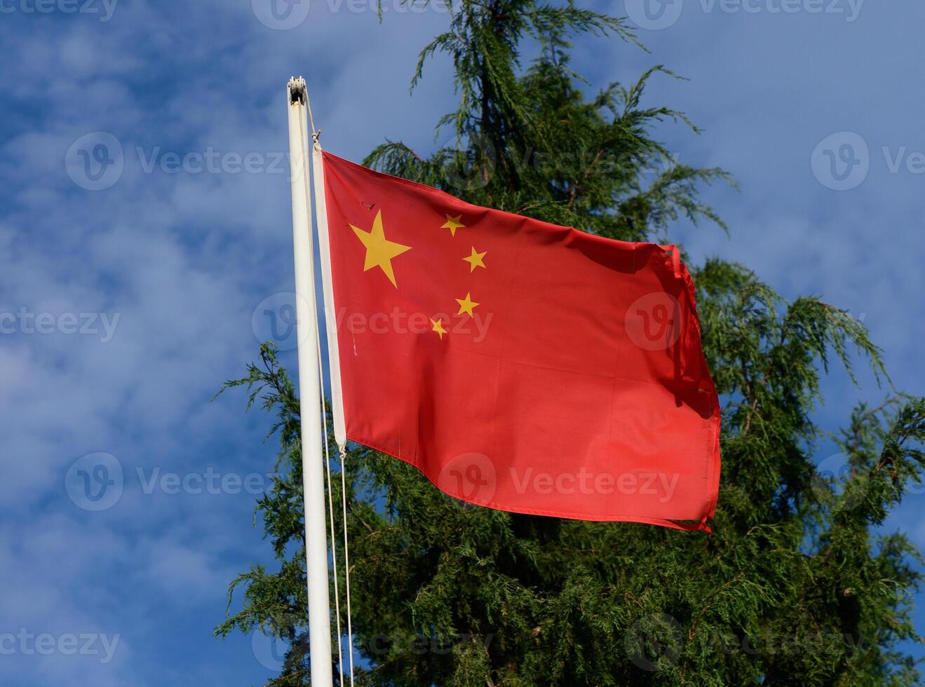 Waving Chinese flag against a backdrop of blue sky and evergreen trees on a bright sunny day photo