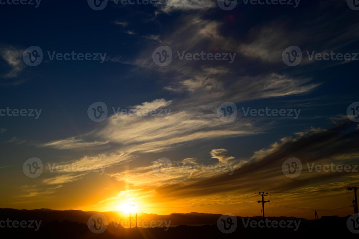 Breathtaking sunset paints the sky with vibrant colors over distant hills and silhouettes of utility poles photo