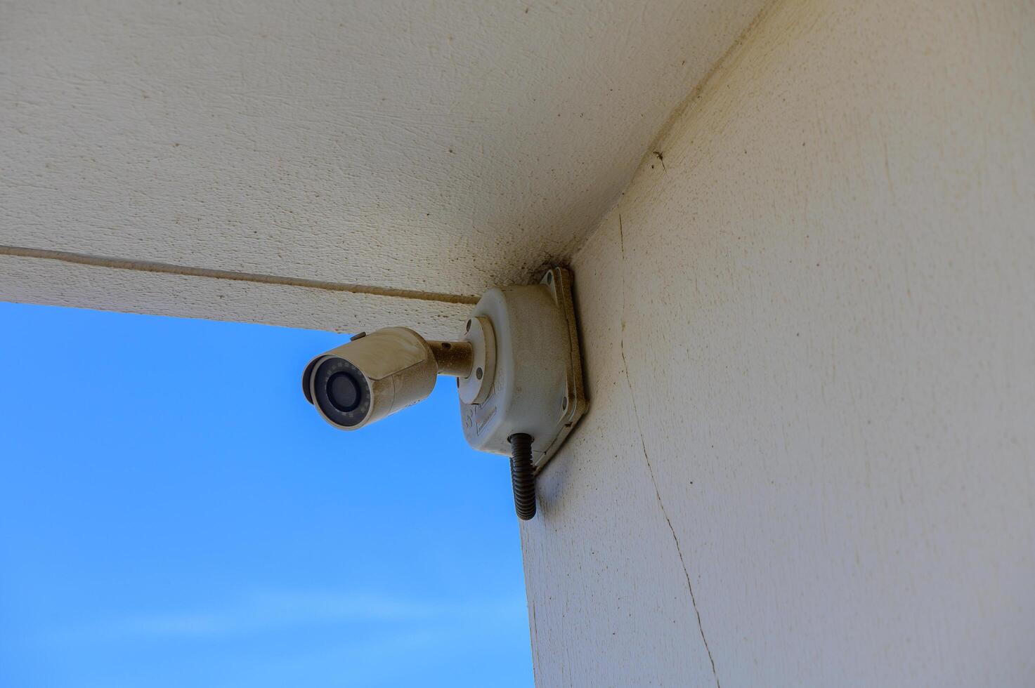 A Surveillance Camera Mounted on a Wall Overlooking a Clear Blue Sky, Capturing Moments in an Outdoor Setting With a Hint of Tranquility photo