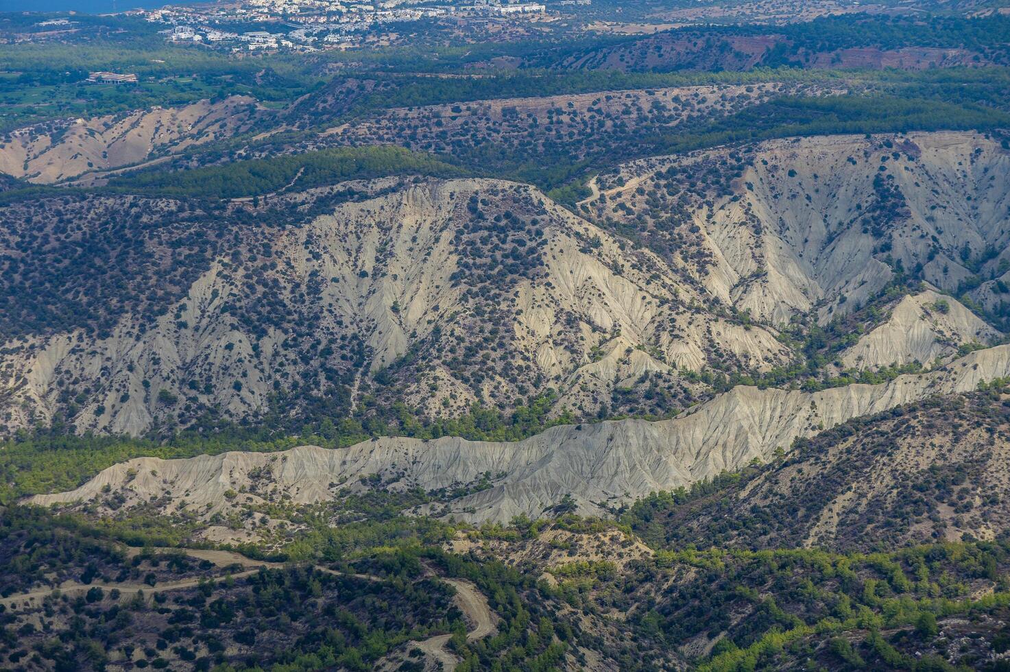 Aerial view of rugged mountain slopes with lush vegetation near a coastal city in Cyprus during daylight hours photo