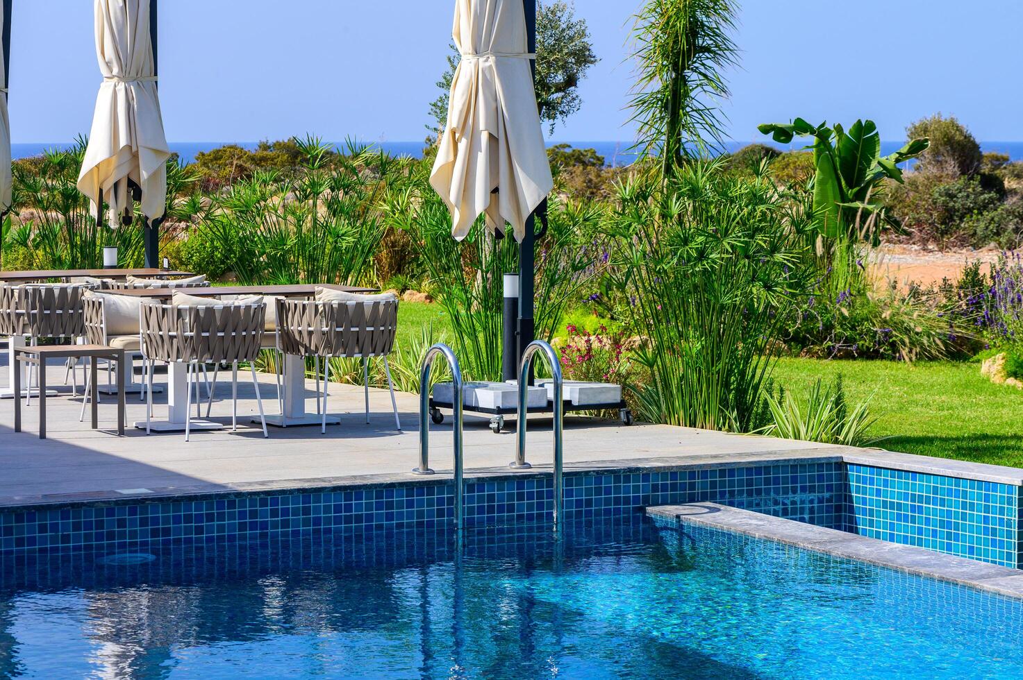 Sunny outdoor swimming pool with comfortable lounge chairs and a scenic garden view near the coast photo