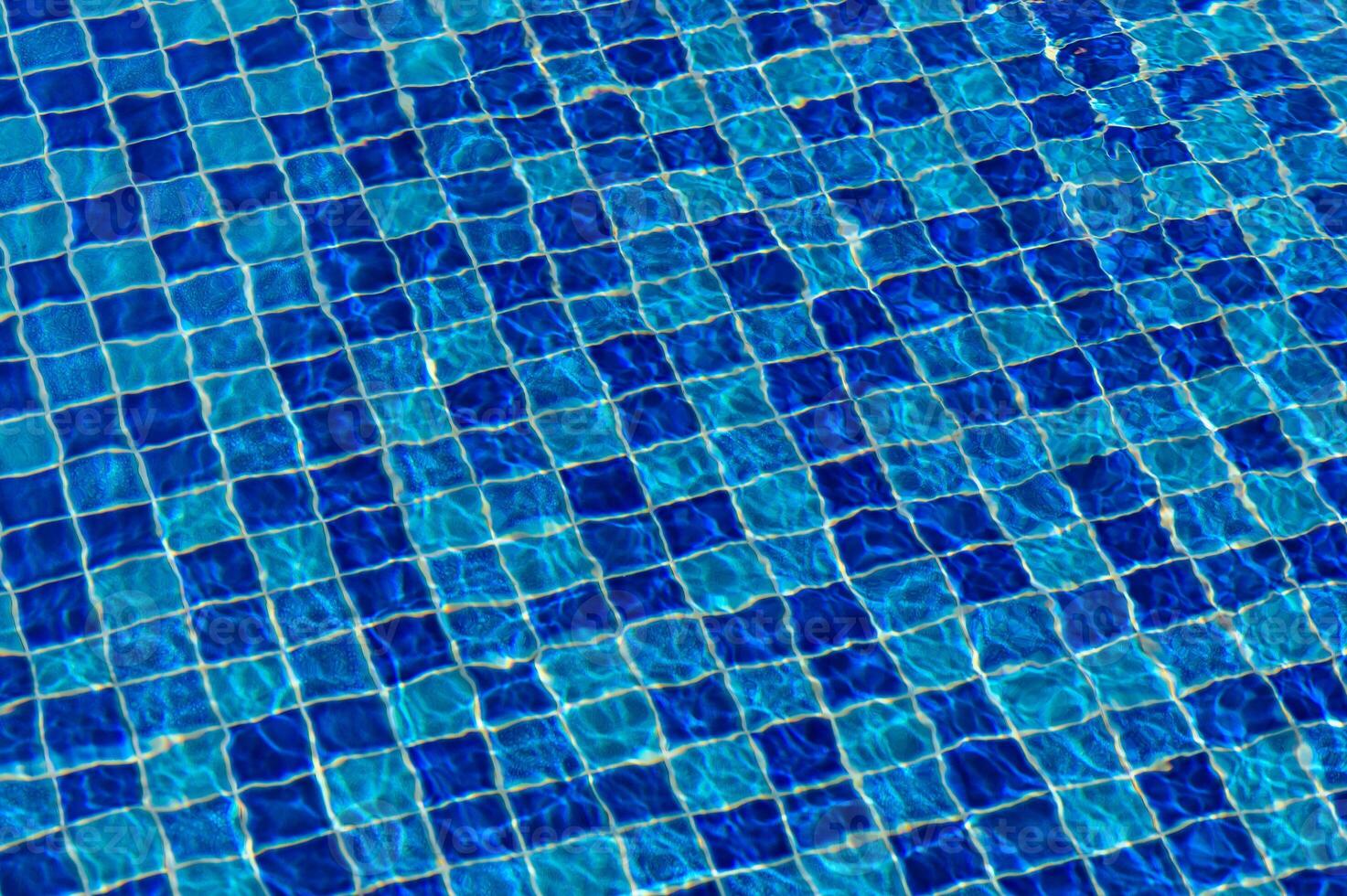Rippling blue water reflects sunlight through tile patterns in a tranquil swimming pool on a sunny day photo