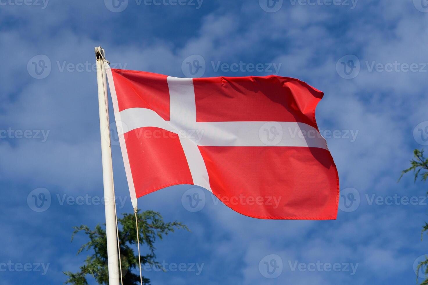 Waving Danish national flag against a backdrop of blue sky and fluffy clouds during a sunny day in Denmark photo