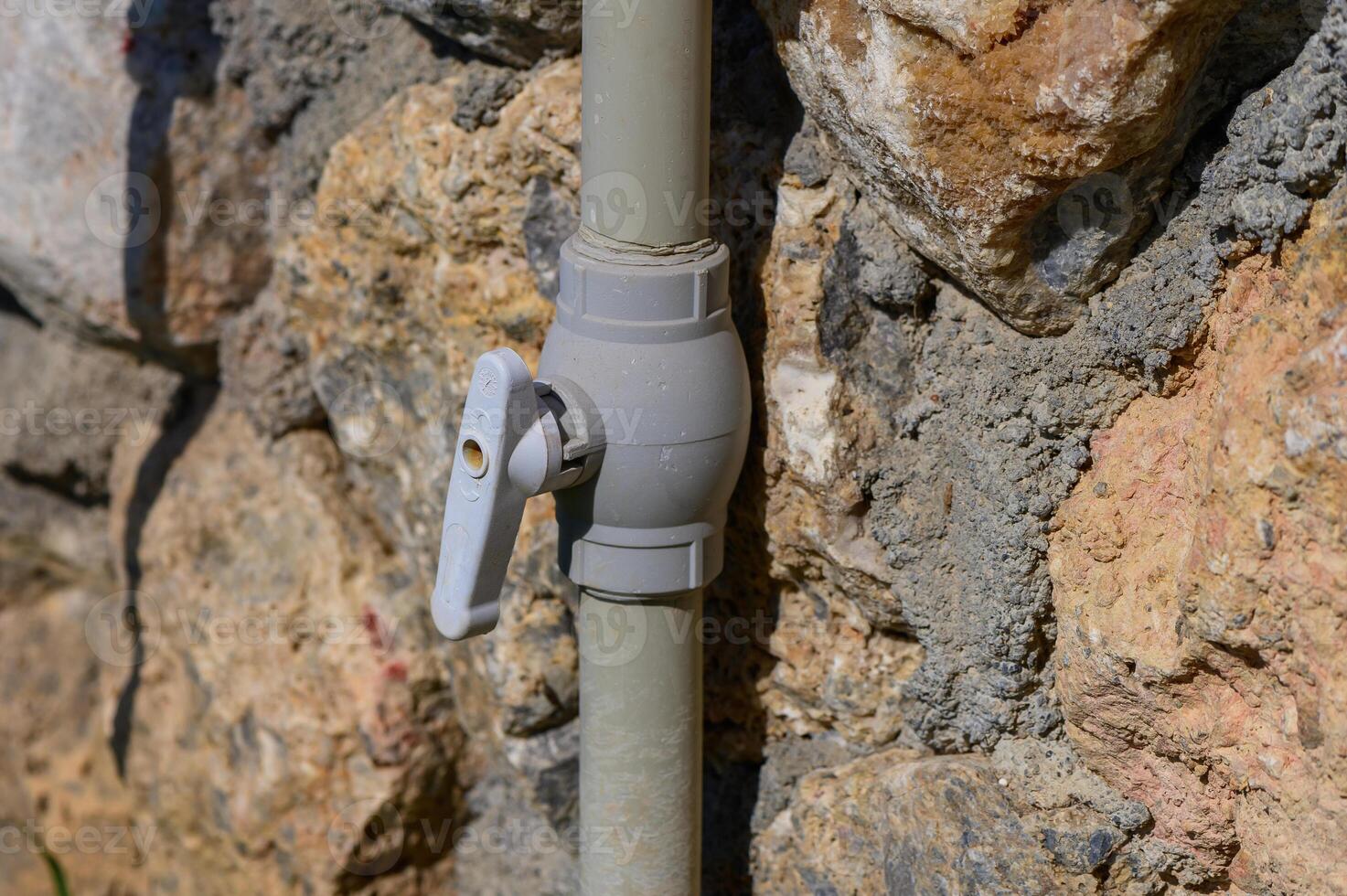 A close-up of a gray valve attached to a stone wall, reflecting sunlight in a tranquil outdoor setting photo