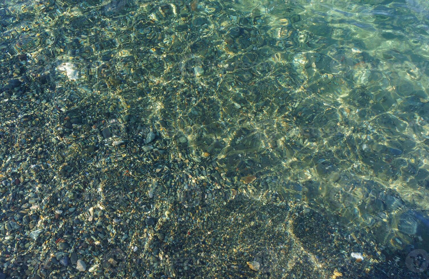 Gentle Waves Lap Over Smooth Pebbles in a Tranquil Shallow Lagoon Under the Bright Sunlight photo