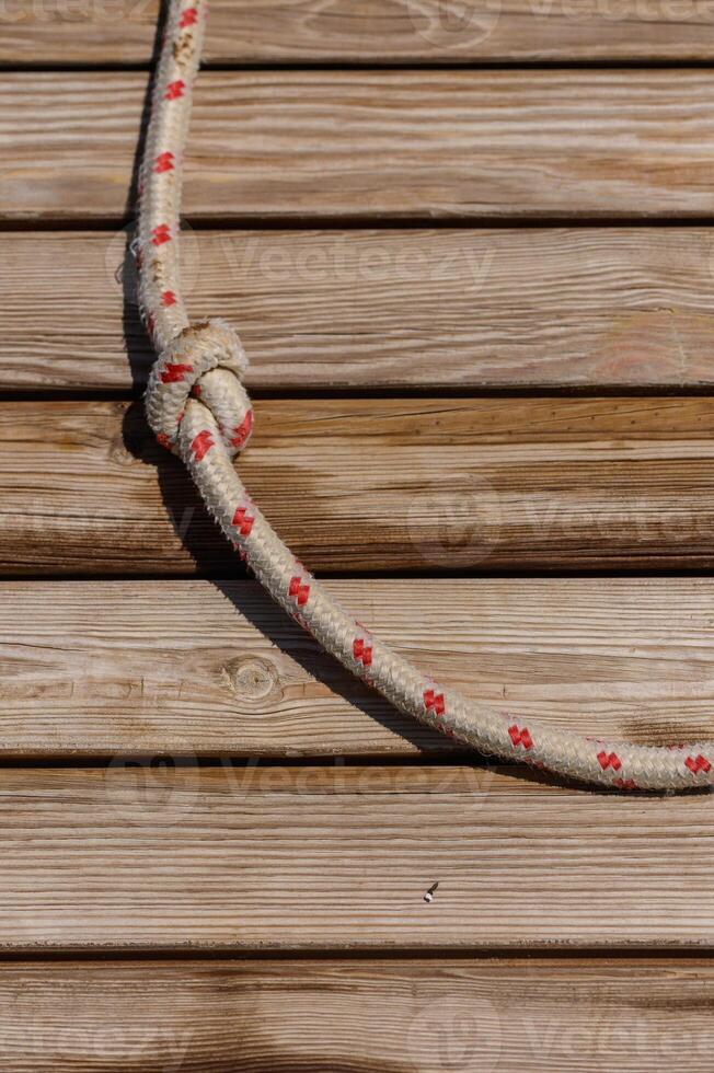 A close-up view of a taut rope with red markings coiled around wooden planks, bathed in warm sunlight on a tranquil afternoon photo