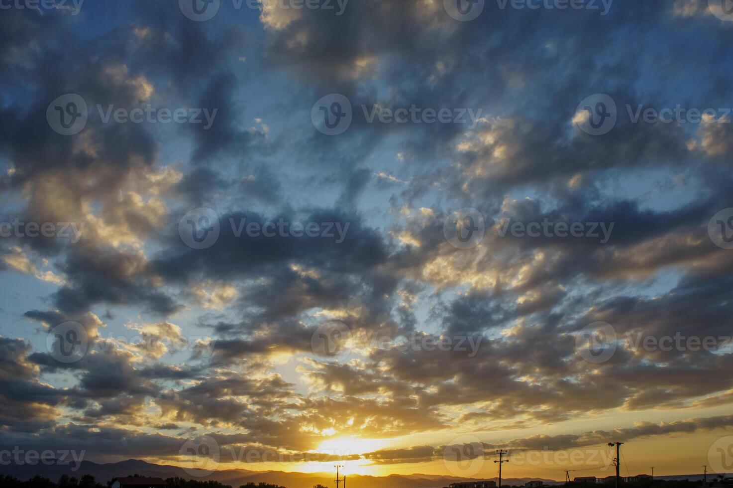 Majestic sunset envelops the horizon with vibrant clouds and golden hues over rural landscape during early evening hours photo