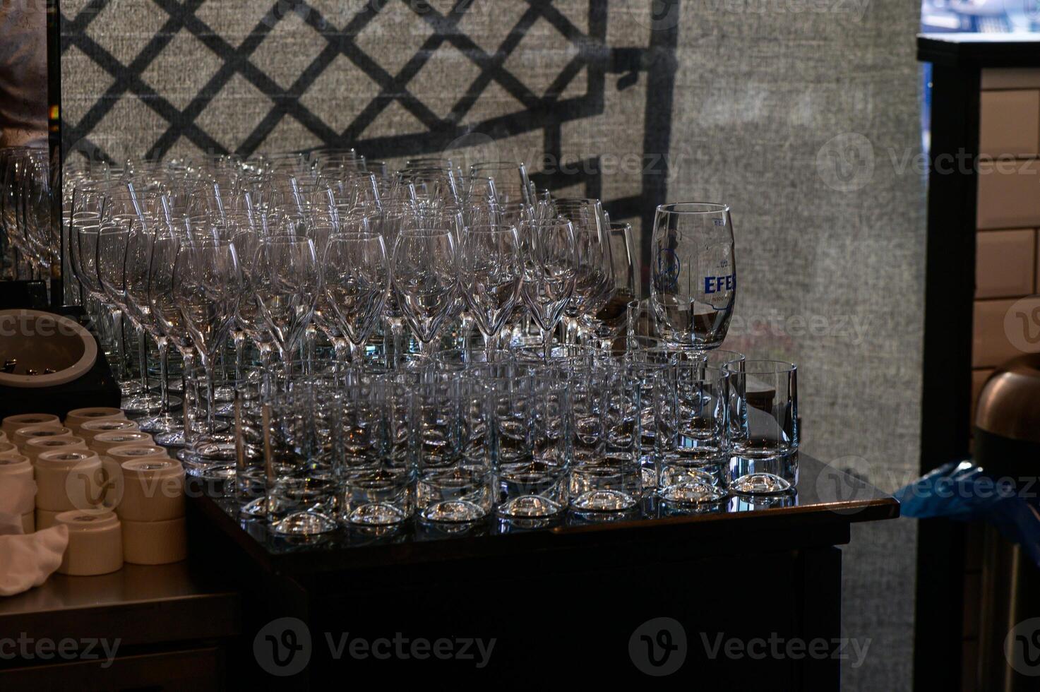 A collection of clear glassware neatly arranged on a wooden counter in a busy restaurant during evening service photo