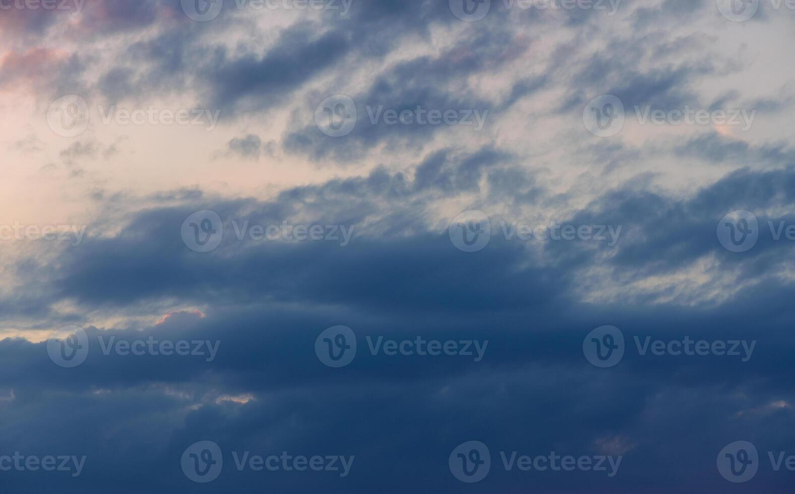 Dramatic cloud formations adorn the evening sky, blending soft hues of blue and gray near the horizon at dusk photo