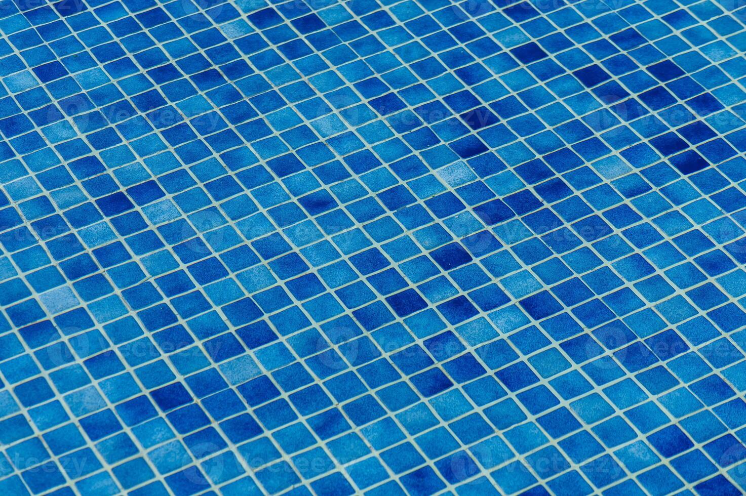 Vibrant blue mosaic tiles arranged in a geometric pattern around a swimming pool on a sunny day photo