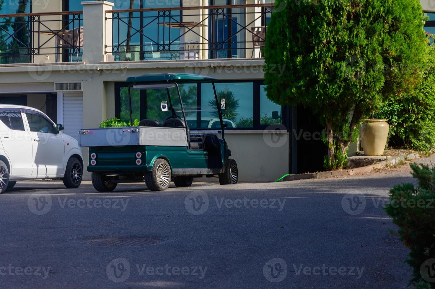 A green utility vehicle parked beside a modern building under the clear blue sky in a serene coastal setting during bright daylight photo