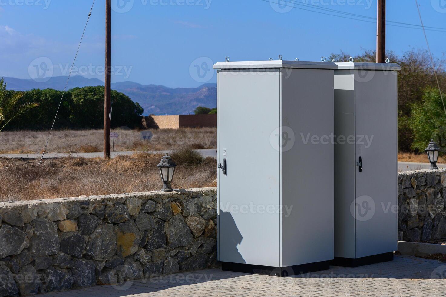 Two utility boxes stand against a backdrop of dry grass and distant mountains on a sunny day photo
