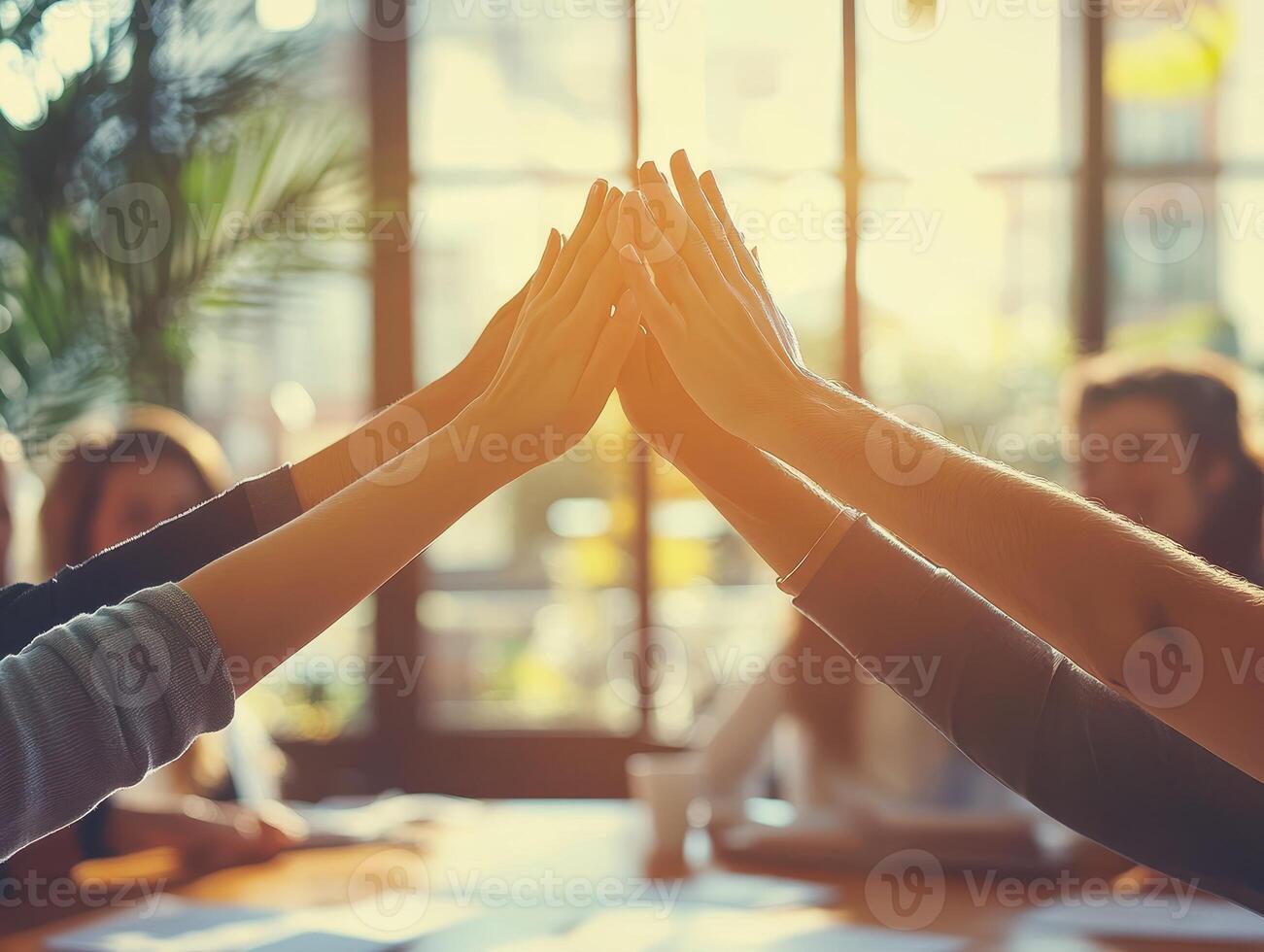 Diverse group of hands reaching together in a collaborative gesture, symbolizing teamwork and unity in a modern office setting with sunlight streaming through large windows. photo