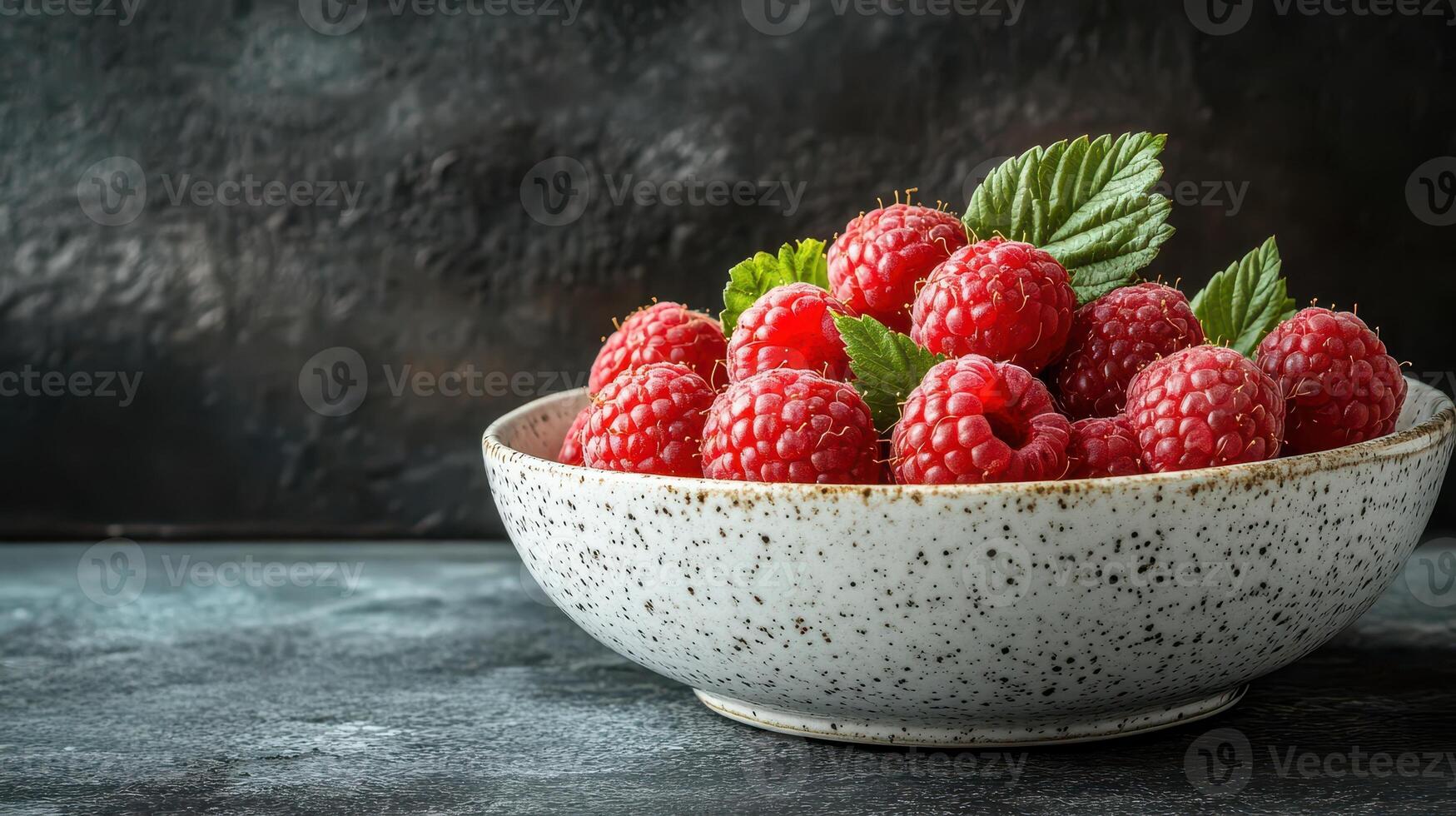 A vibrant bowl filled with fresh raspberries garnished with green mint leaves, set against a dark textured background, showcasing the rich color and freshness of the fruit. photo