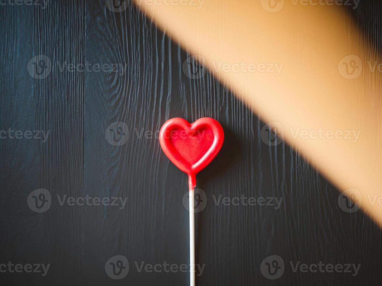 A red heart shaped lollipop on a wooden surface photo