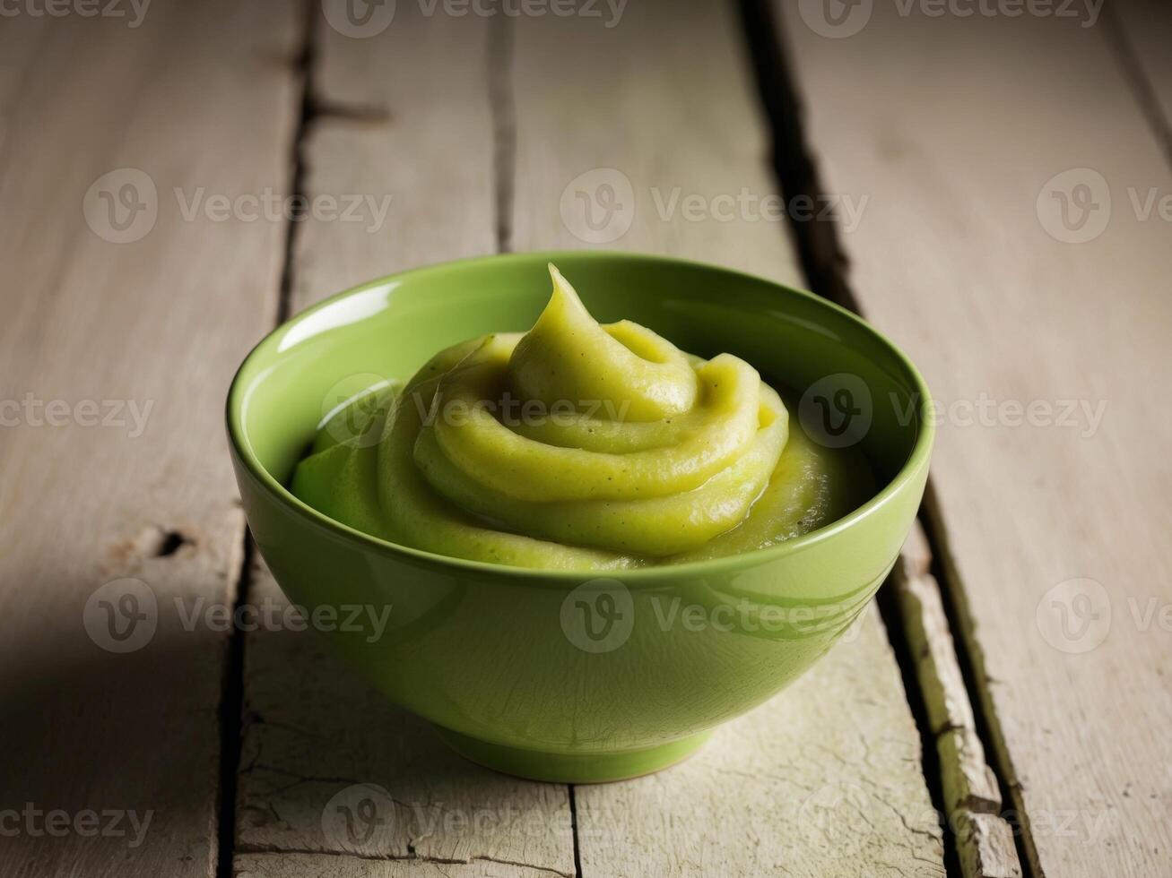 A green bowl of mashed avocado on a wooden table photo