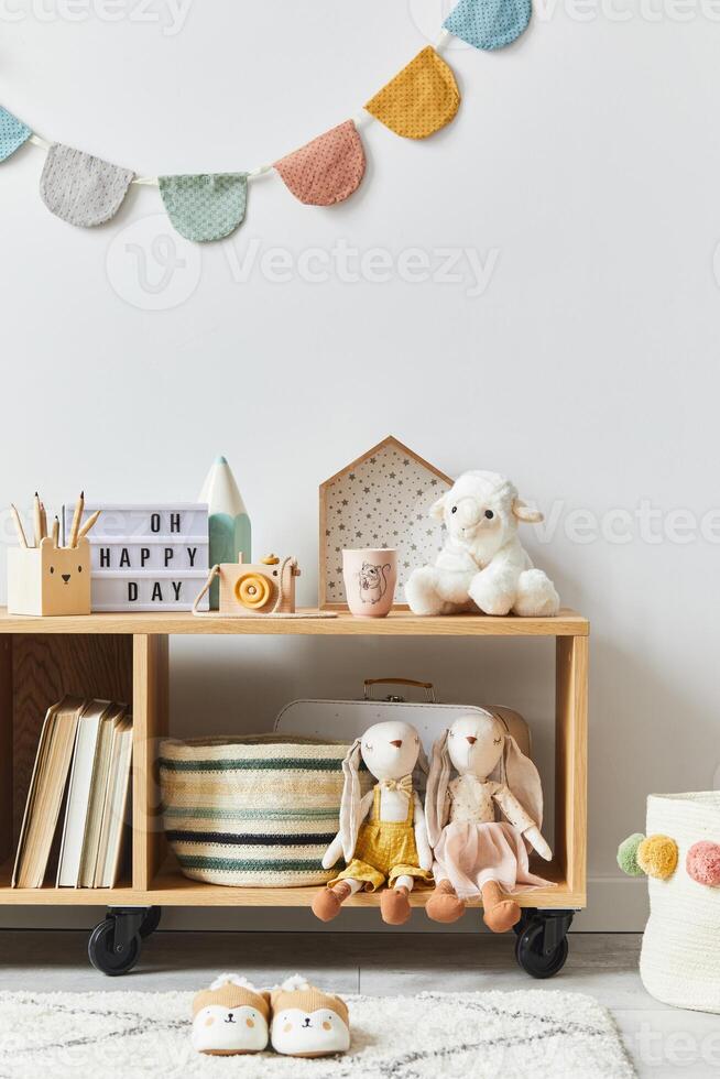 Stylish scandinavian newborn baby room with toys, plush animal, photo camera and accessories. Cozy decoration and hanging cotton balls on the white wall.