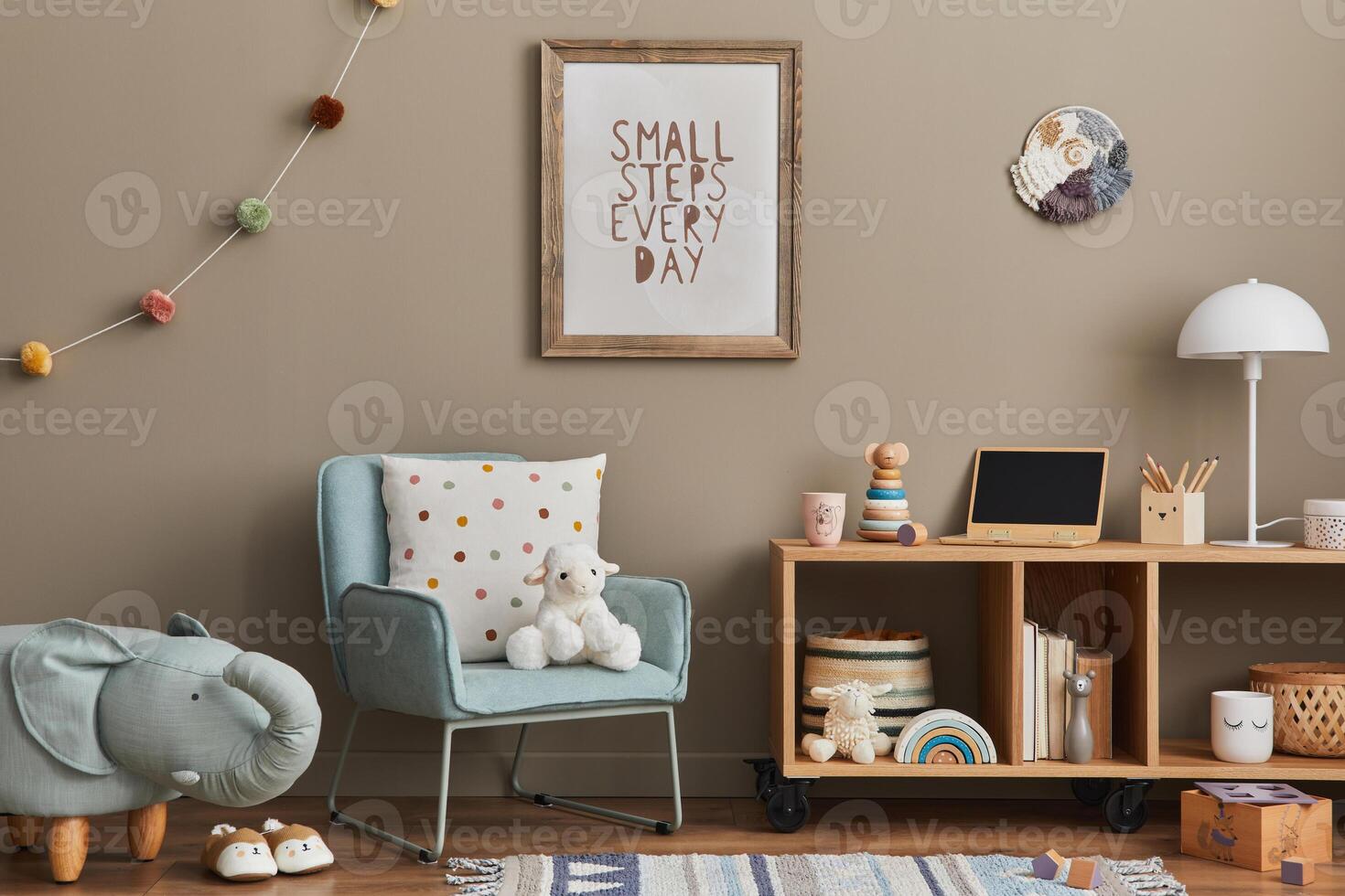 Cozy interior of child room with mint armchair, brown mock up poster frame, toys, teddy bear, decoration and hanging cotton colorful balls. Beige wall. Warm kid space. Template. photo