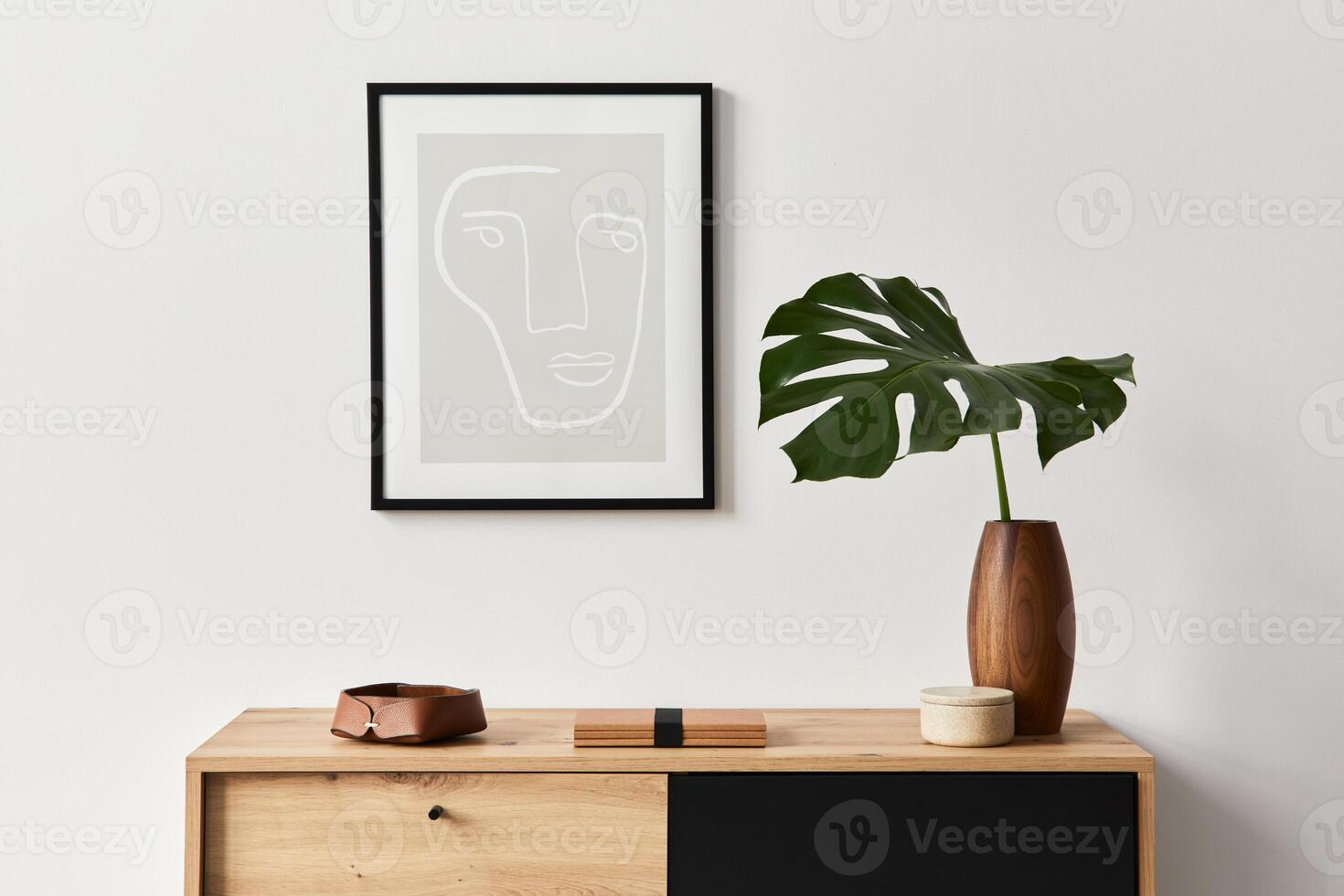 Stylish interior of living room with mock up poster frame, wooden commode, tropical leaf in ceramic vase and elegant personal accessories. Minimalist concept of home decor. photo