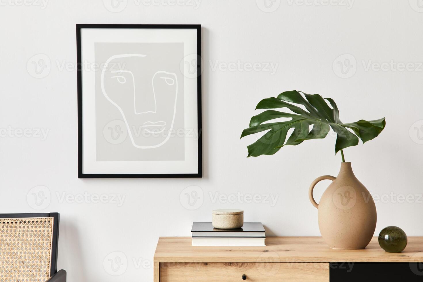 Stylish interior of living room with mock up poster frame, wooden commode, book, tropical leaf in ceramic vase and elegant personal accessories. Minimalist concept of home decor photo